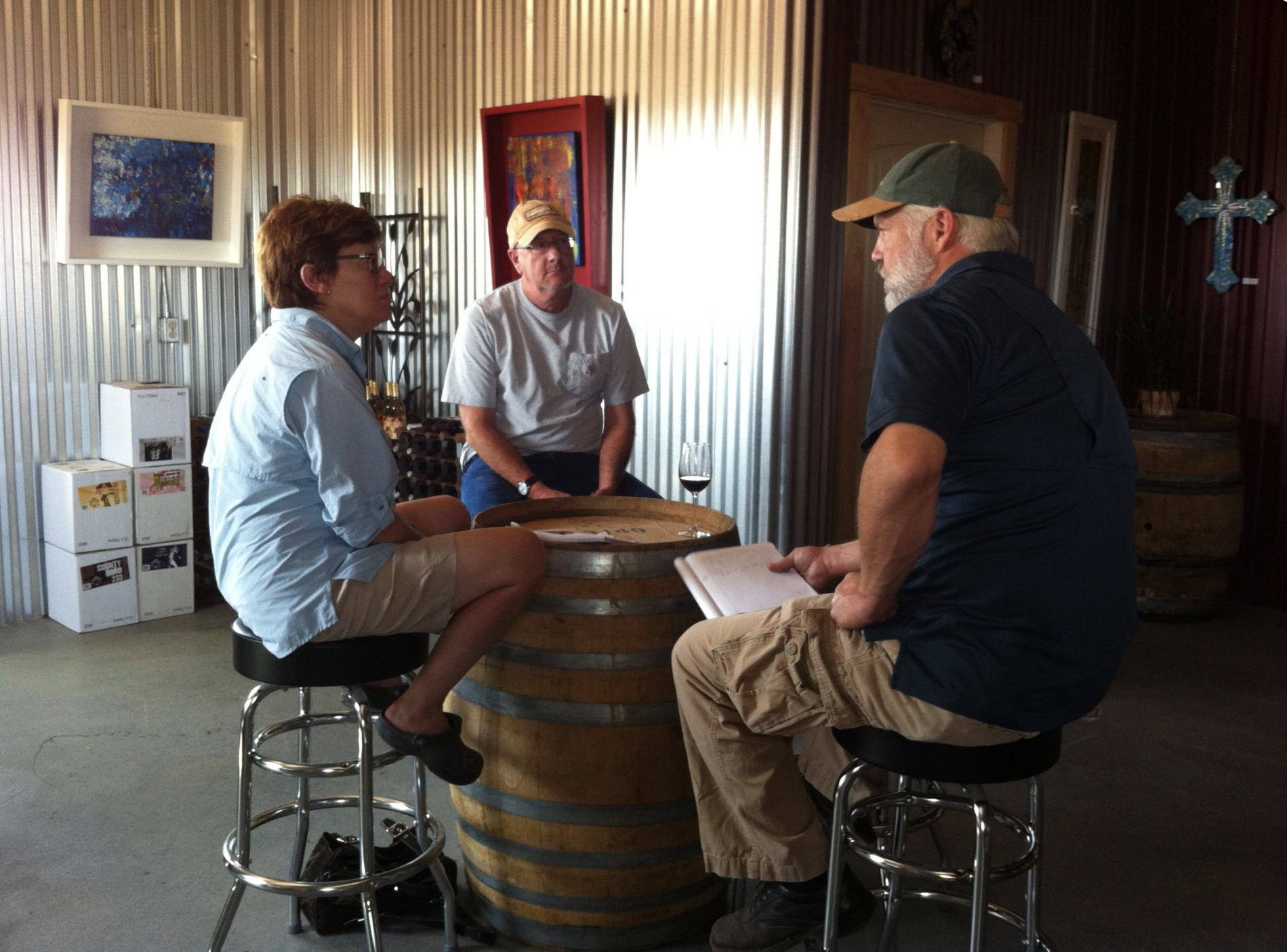 Three people are discussing and sitting around a wine barrel table.