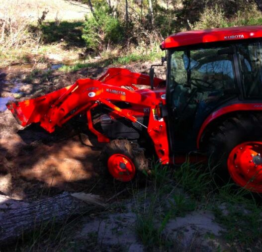 Orange tractor clearing overgrown bushes