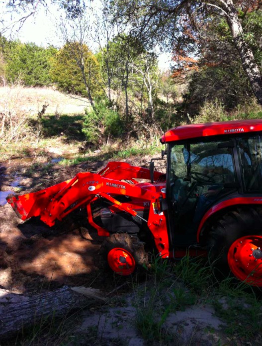 Orange tractor clearing overgrown bushes
